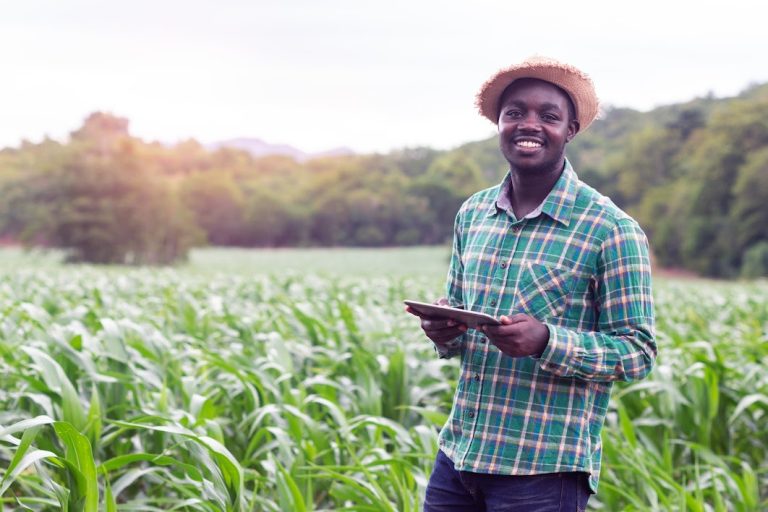 A farmer with tablet, smiling in a field.